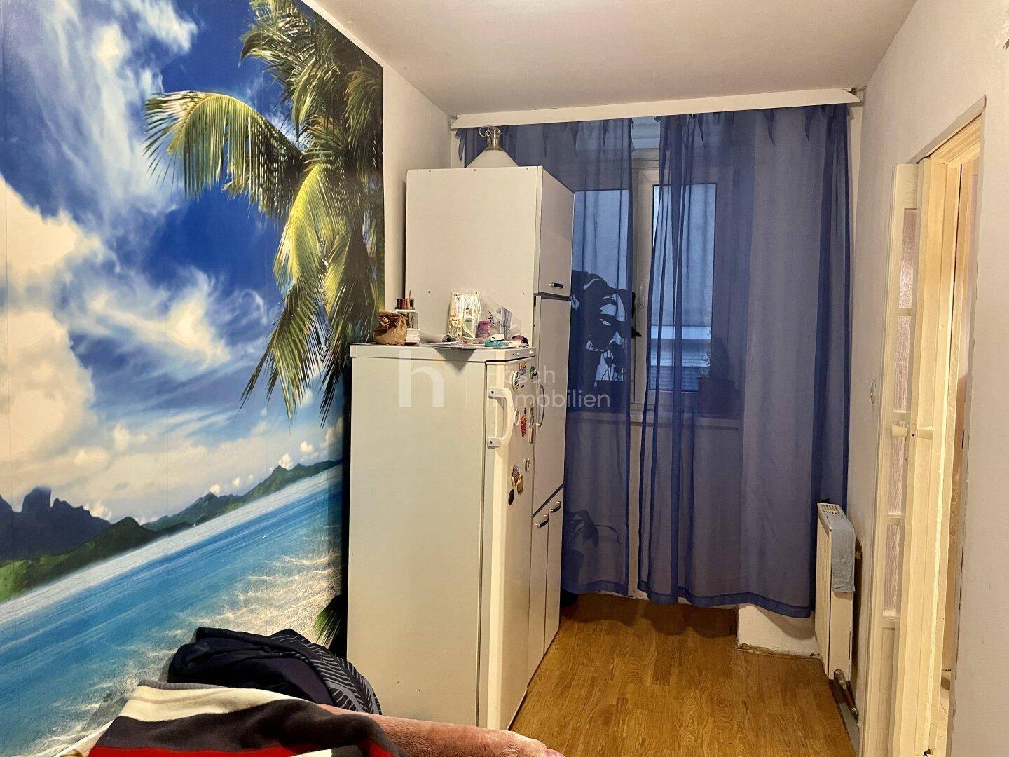 Schlafzimmer mit Kühlschrank, Schrank und tropischer Wandtapete, die eine besondere Atmosphäre schafft.