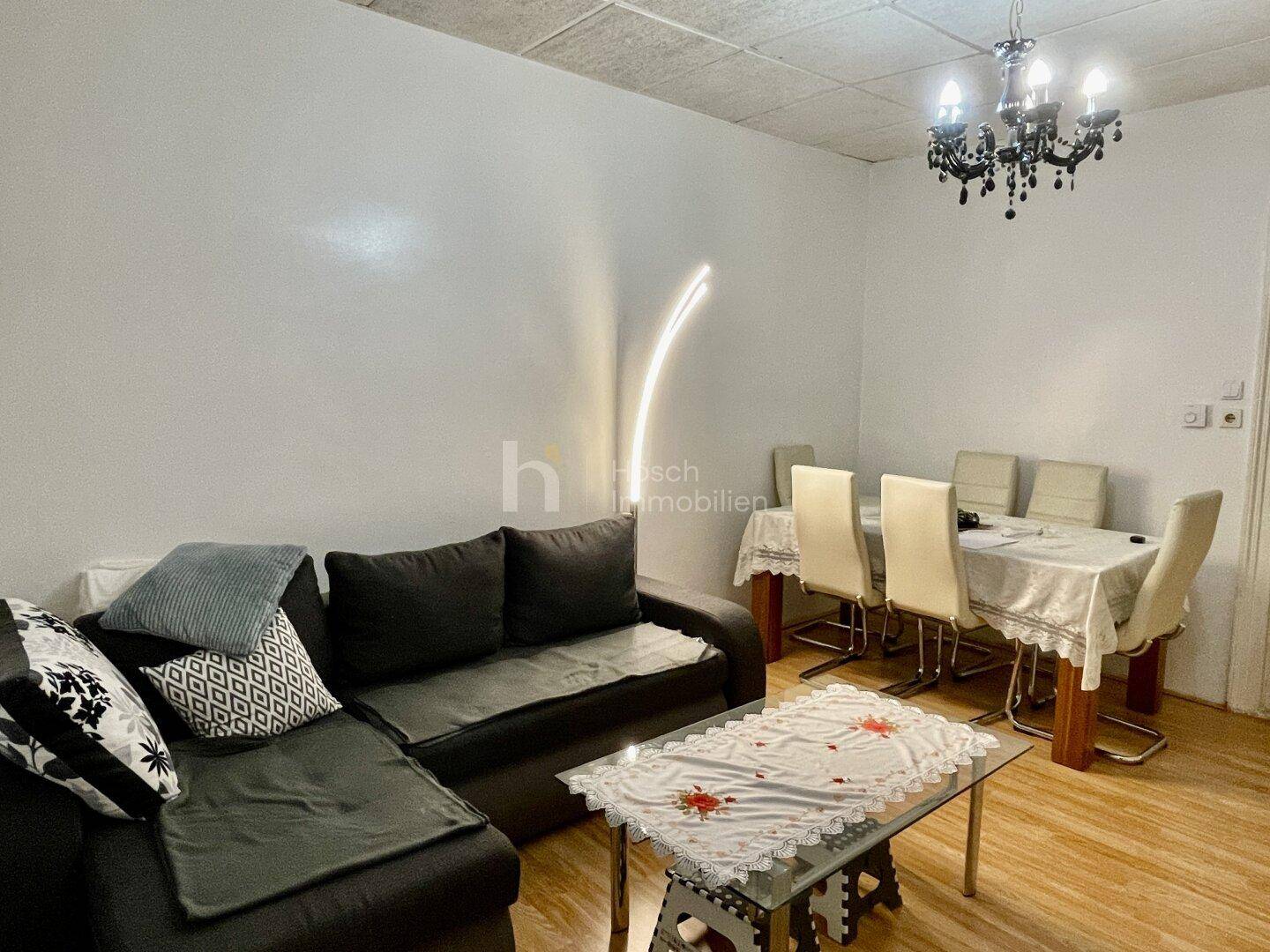 Wohn-Essbereich mit dunklem Sofa, Esstisch und Kronleuchter in einem gemütlichen Ambiente.