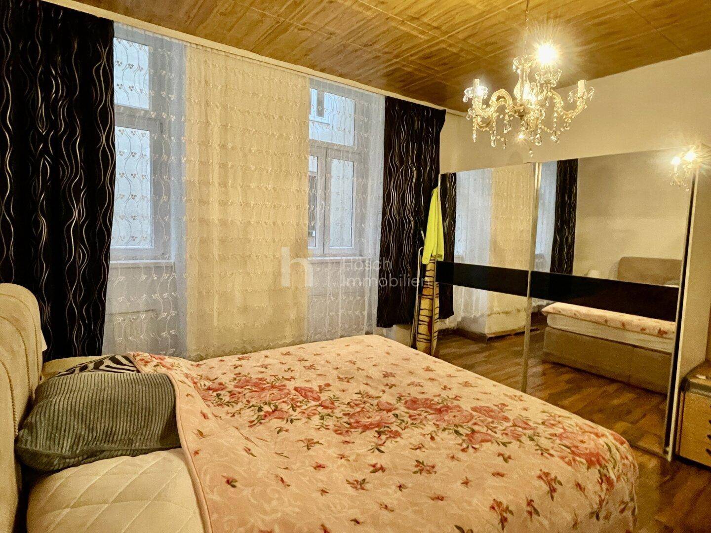 Helles Schlafzimmer mit Doppelbett, Holzbalkendecke und Fenstern mit hellen Vorhängen.