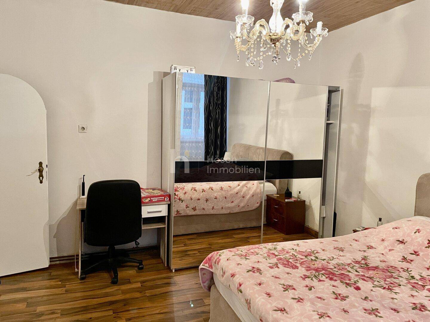 Schlafzimmer mit Spiegelschrank, Schreibtisch und Holzbalkendecke, die Gemütlichkeit verleiht.