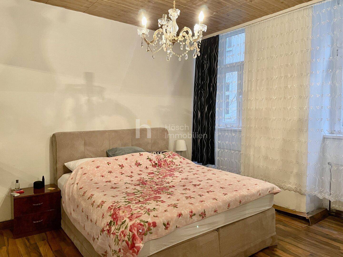Schlafzimmer mit großem Bett, Holzbalkendecke und einem eleganten Kronleuchter.
