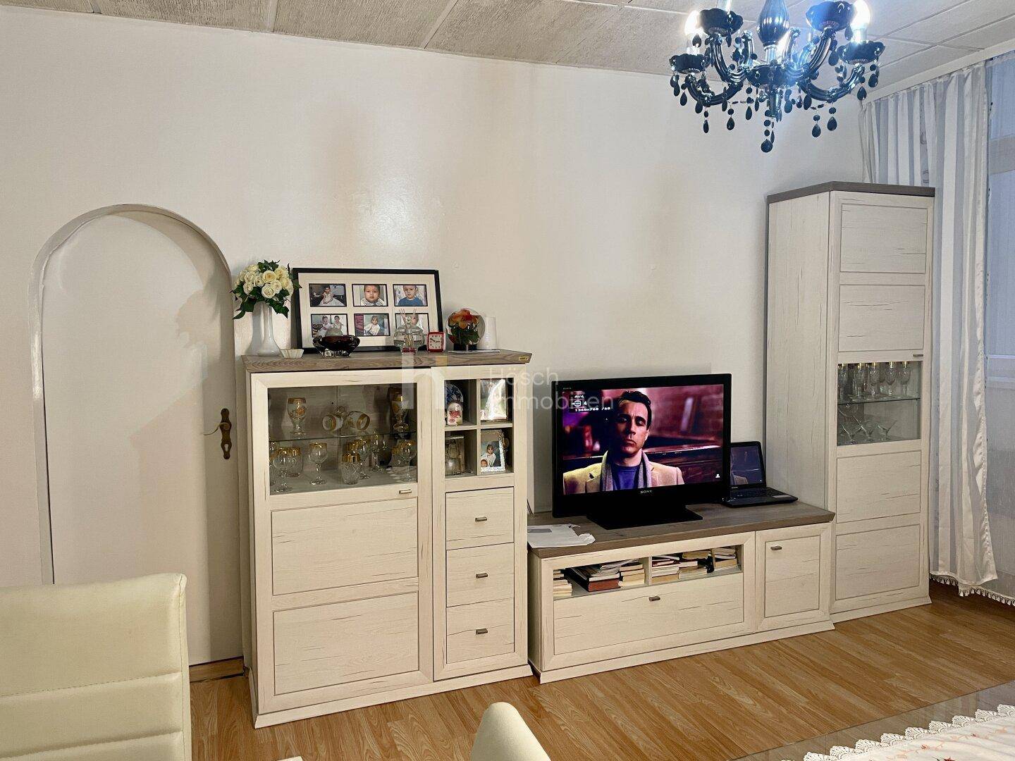 Wohnbereich mit TV-Möbeln, Vitrine und einem dekorativen Kronleuchter an der Decke.