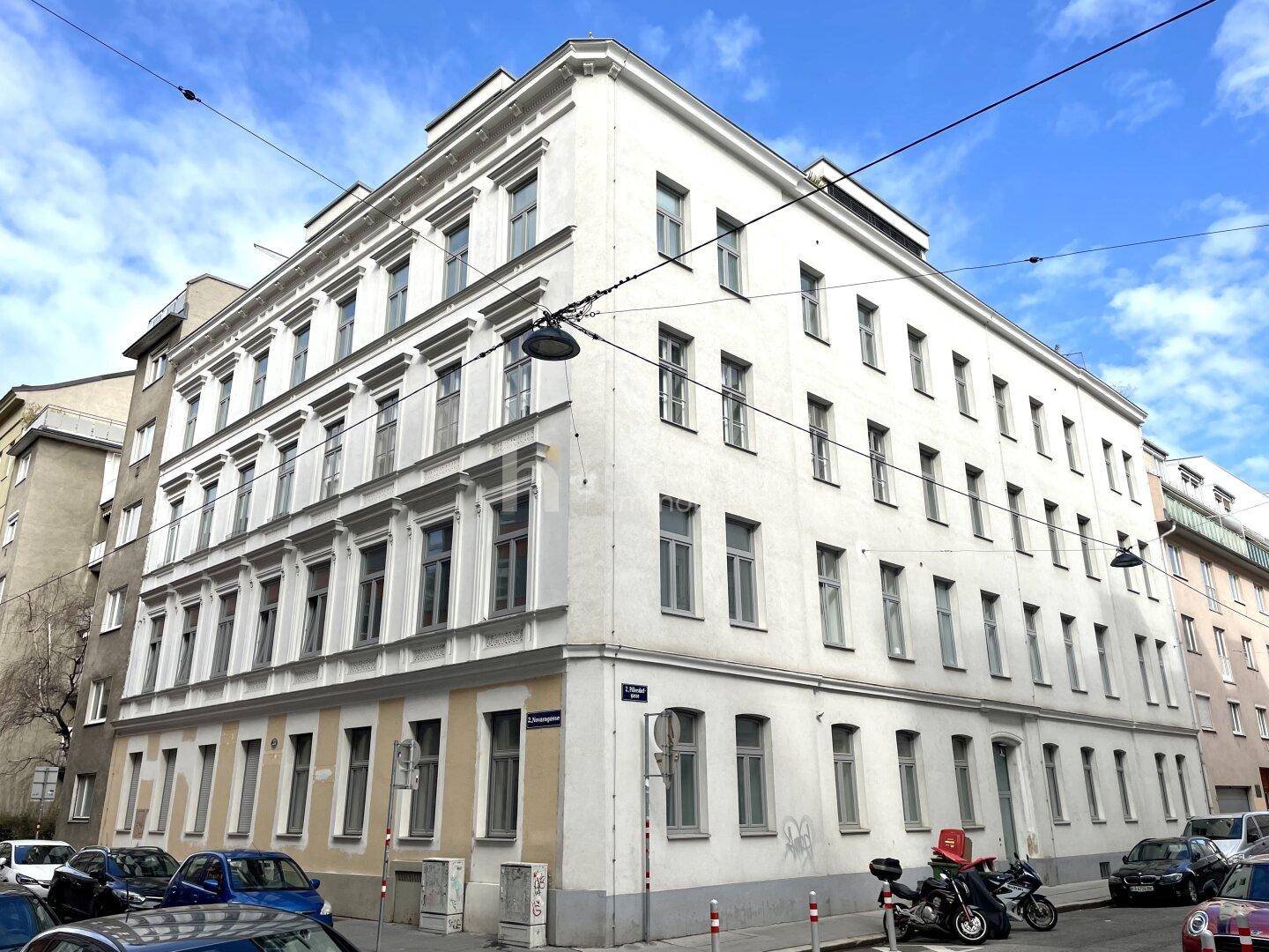 Klassisches Eckgebäude mit vielen Fenstern und traditioneller Architektur an einer belebten Stadtstraße.