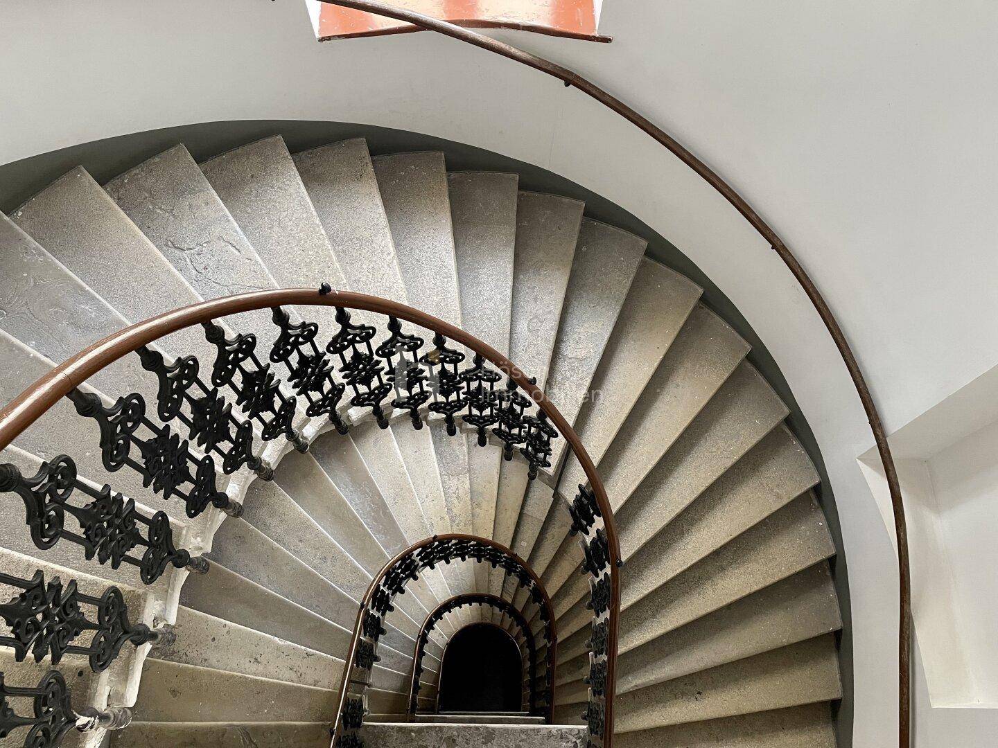 Blick von oben auf eine elegante Wendeltreppe mit Steinstufen und kunstvollem schmiedeeisernem Geländer.
