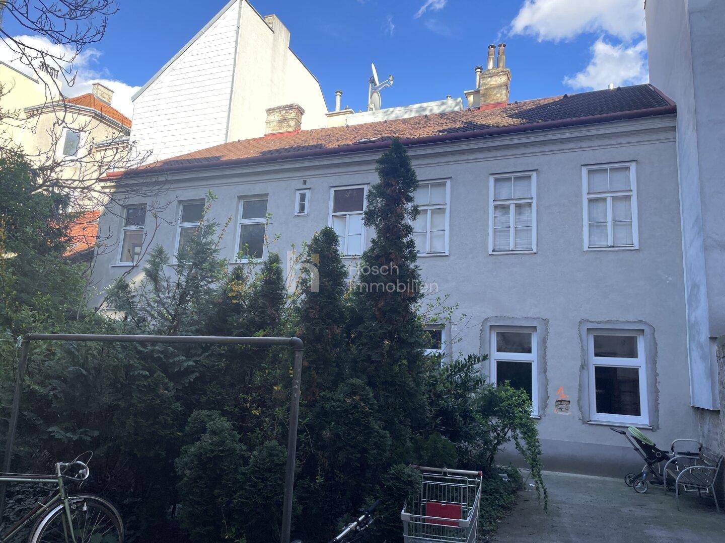 Rückansicht eines Altbaus von einem begrünten Innenhof mit Bäumen und Sträuchern.