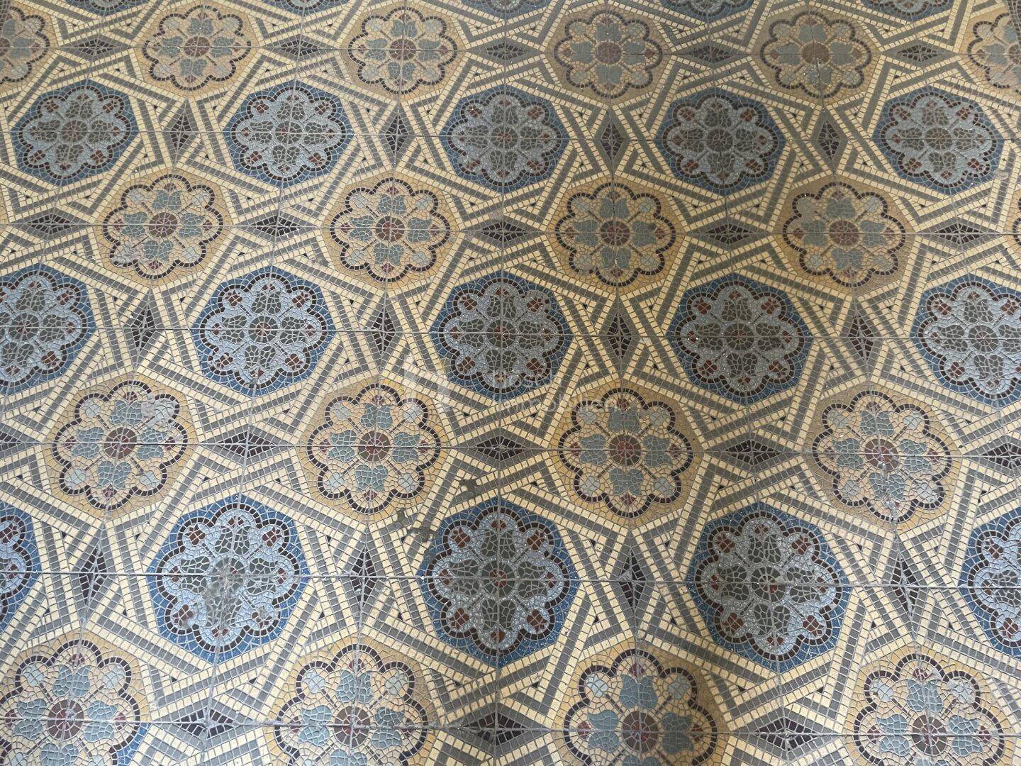Historischer Mosaikfliesenboden mit floralen und geometrischen Mustern in Blautönen.