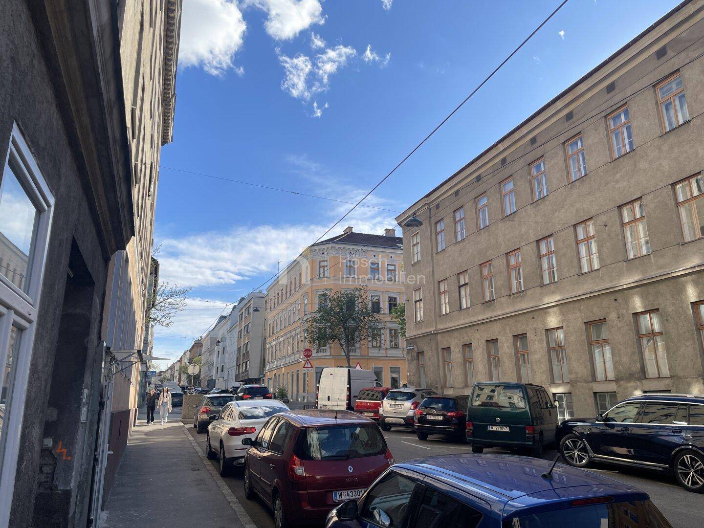 Städtische Straße mit parkenden Autos und Altbauten unter blauem Himmel.