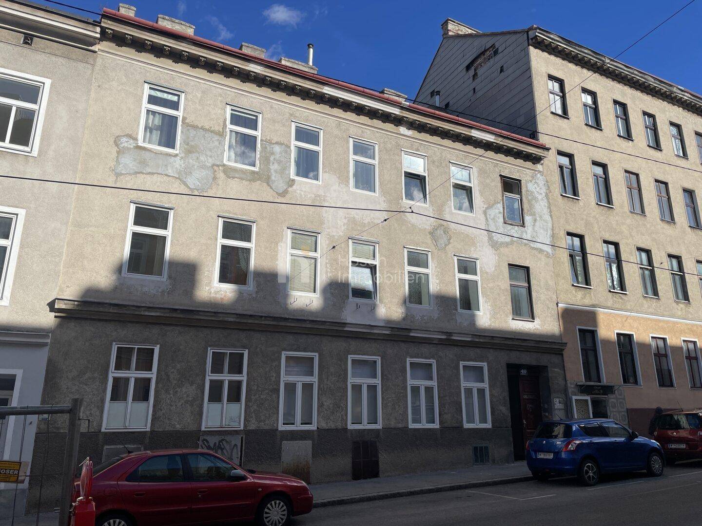 Fassade eines Altbaus an einer städtischen Straße mit parkenden Autos.