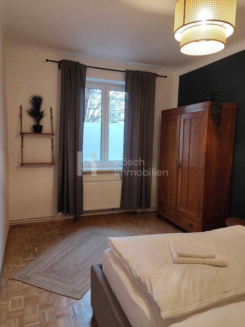 Helles Schlafzimmer mit Fenster, Holzboden und einem großen Kleiderschrank aus Holz.
