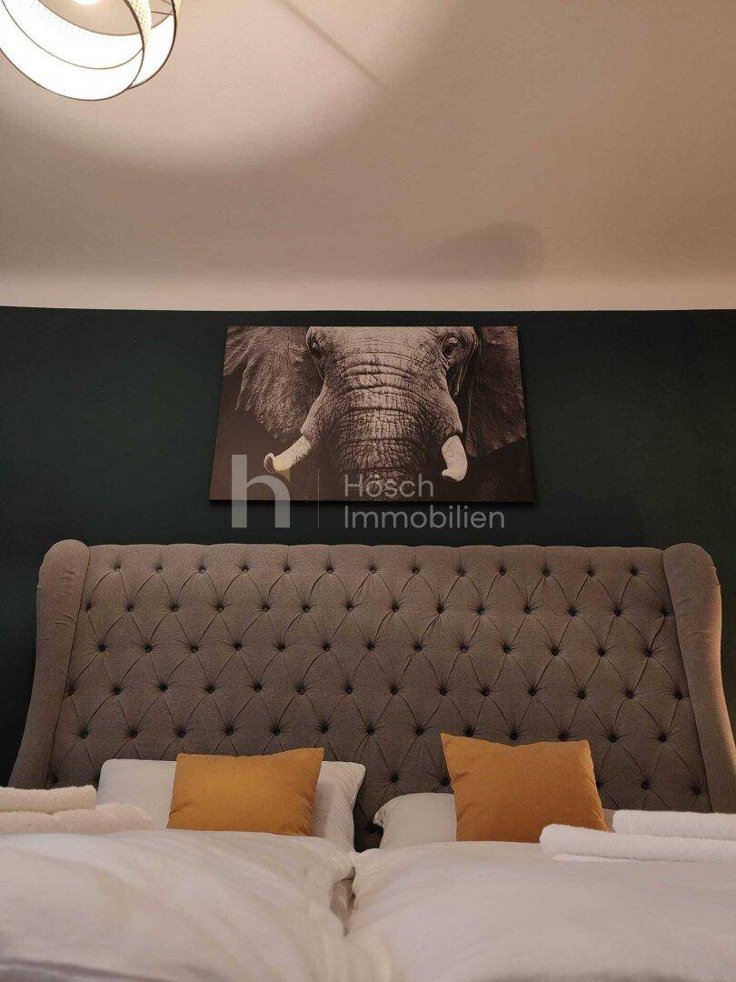 Detailansicht des gepolsterten Bettes mit hoher Kopflehne und Elefantenbild an der Wand.