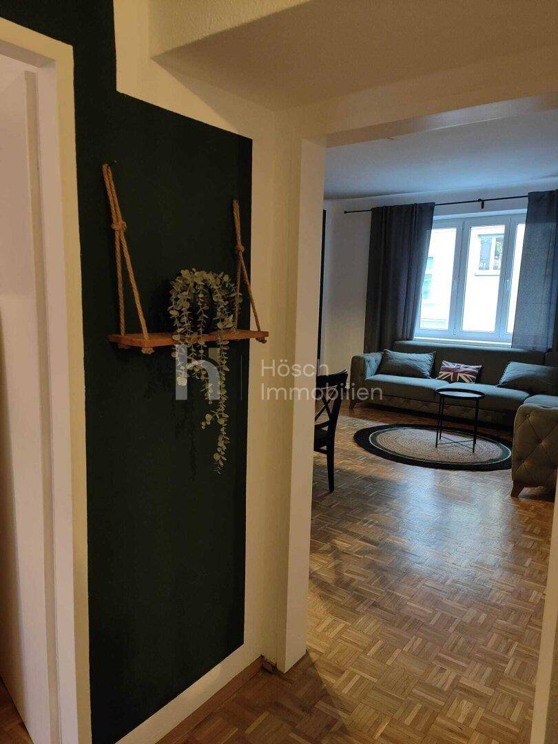 Flur mit dunkler Akzentwand und Blick in den Wohnbereich mit Sofa und Fenster.