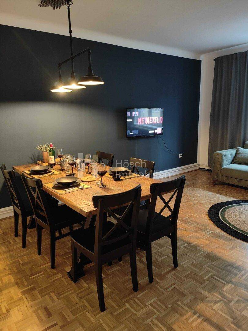 Geräumiger Wohn-Essbereich mit großem Holztisch, Fernseher und dunkler Akzentwand.