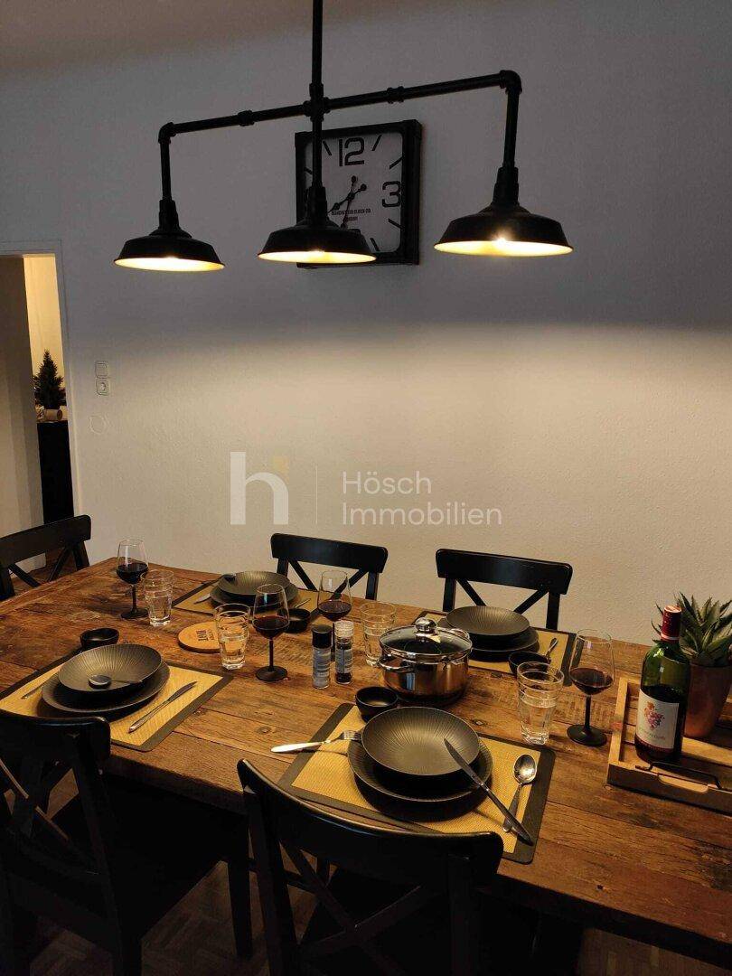 Esstisch mit moderner Hängelampe und Wanduhr, bereit für ein gemütliches Essen.