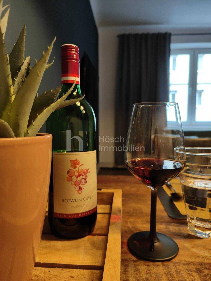 Detailaufnahme von Rotwein und einem Glas auf dem Holztisch, mit Fenster im Hintergrund.