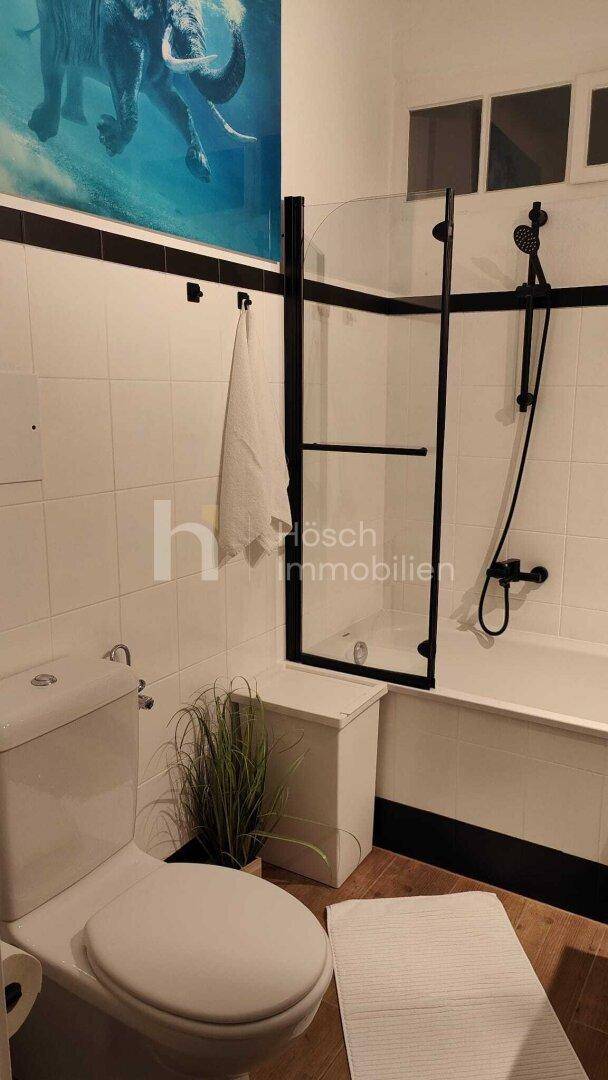 Badezimmer mit Toilette, Badewanne und Duschabtrennung, sowie Fliesen an den Wänden.