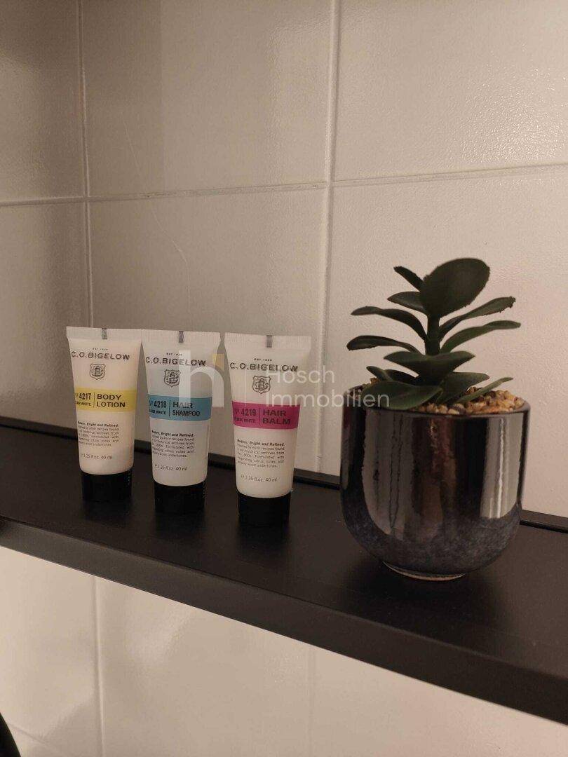 Detailaufnahme von Pflegeprodukten und einer kleinen Pflanze auf einem Regal im Badezimmer.