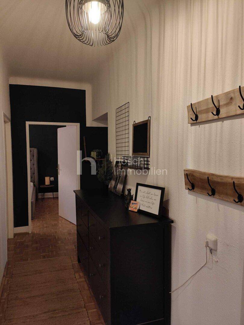 Langer Flur mit Kommode, Garderobenhaken und Blick in ein angrenzendes Zimmer.