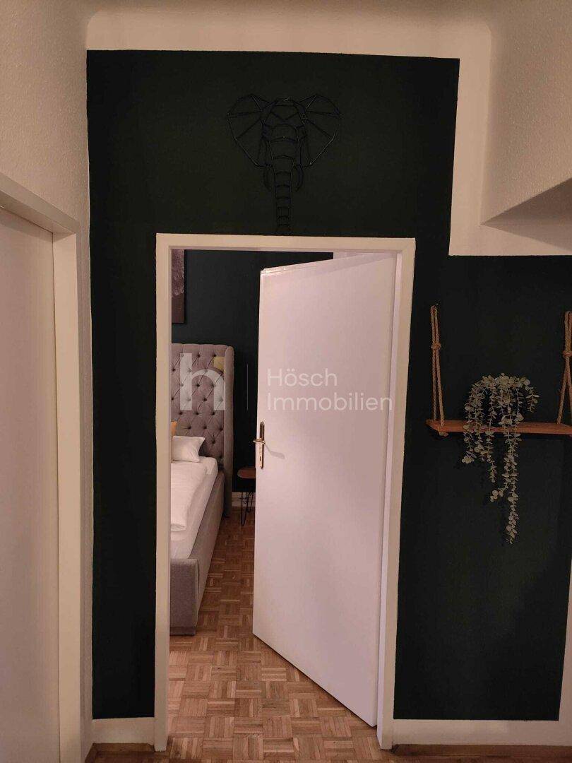 Eingangsbereich mit dunkler Akzentwand und offener Tür, die in ein Schlafzimmer führt.