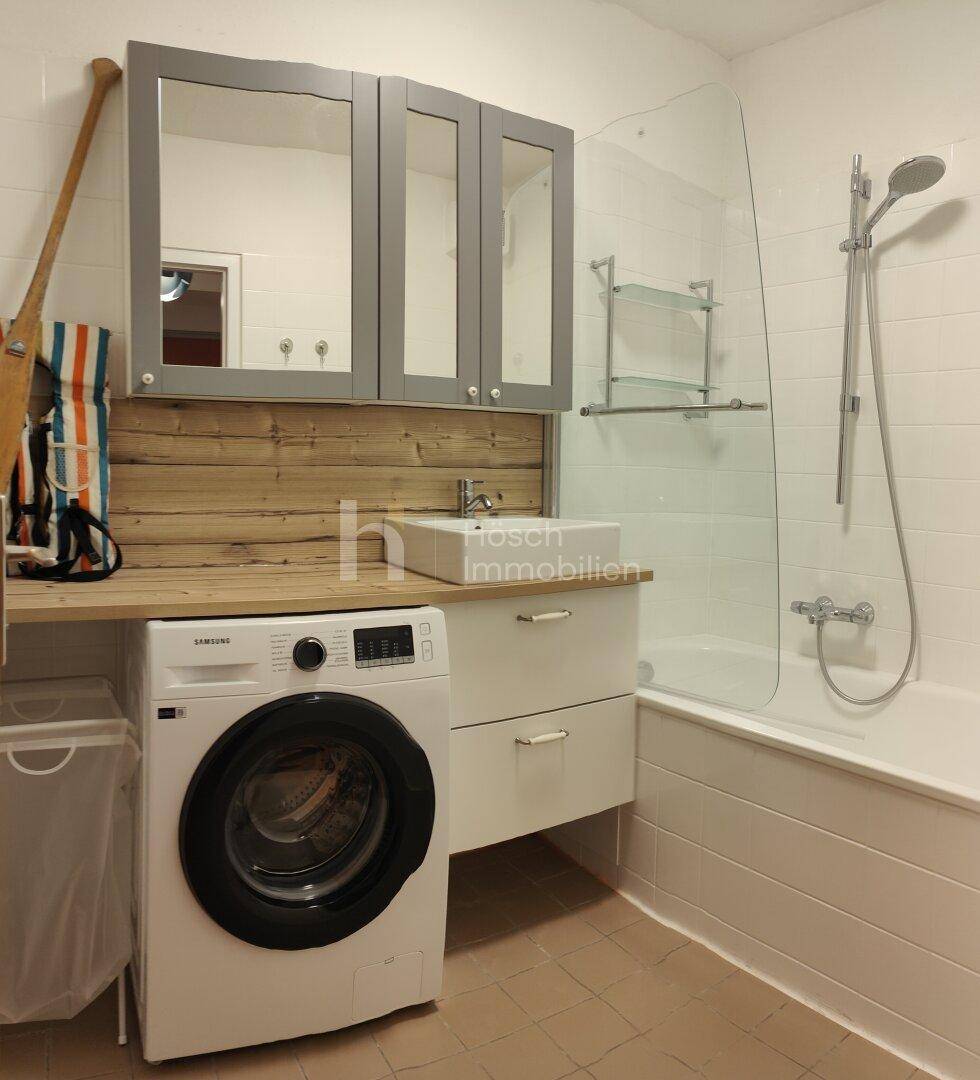 Modernes Badezimmer mit Badewanne, Dusche, Waschmaschine und einem Waschbecken mit Holzablage.