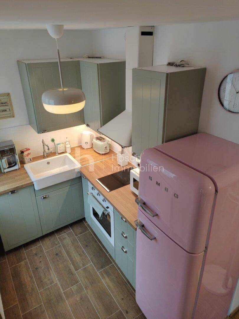 Kompakte Küche mit hellgrünen Schränken, Holzarbeitsplatte und einem auffälligen rosa Kühlschrank.