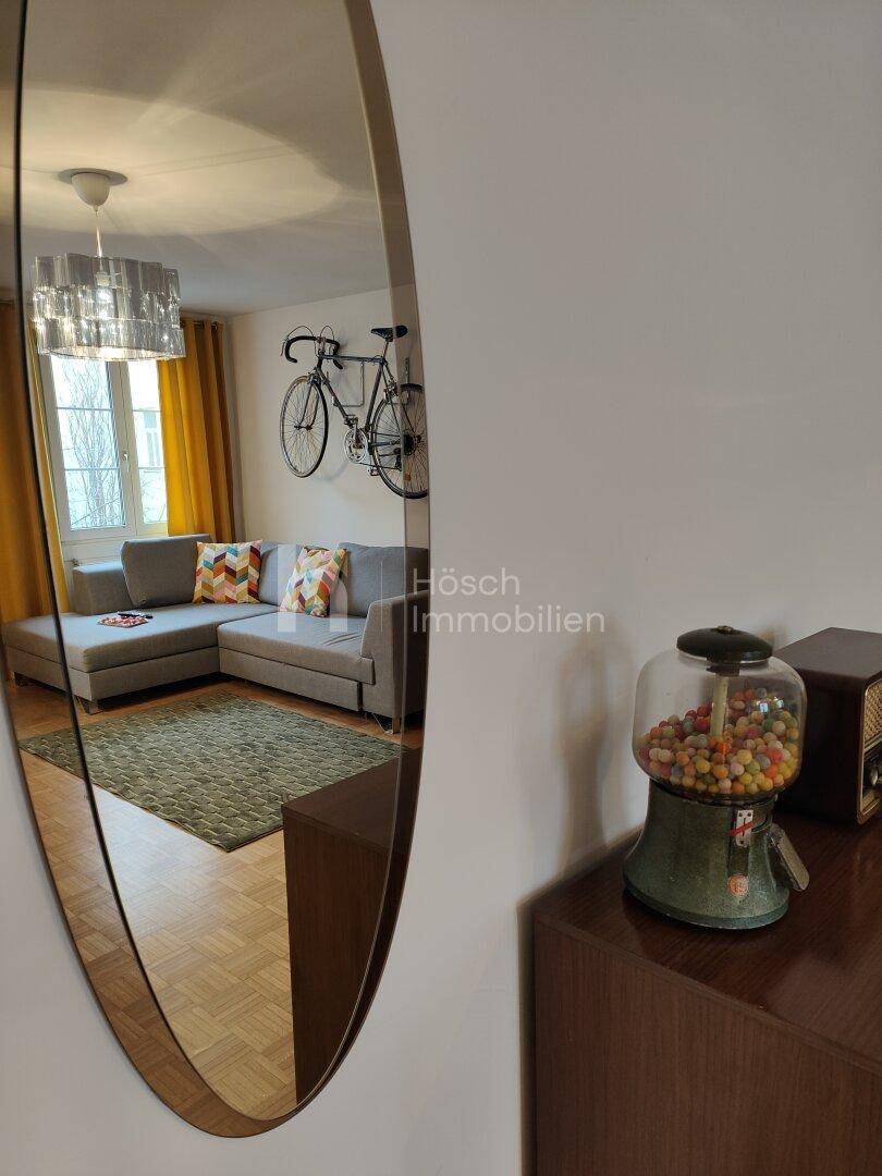 Spiegelreflexion des Wohnzimmers mit Sofa, Fahrrad an der Wand und einem modernen Deckenlicht.