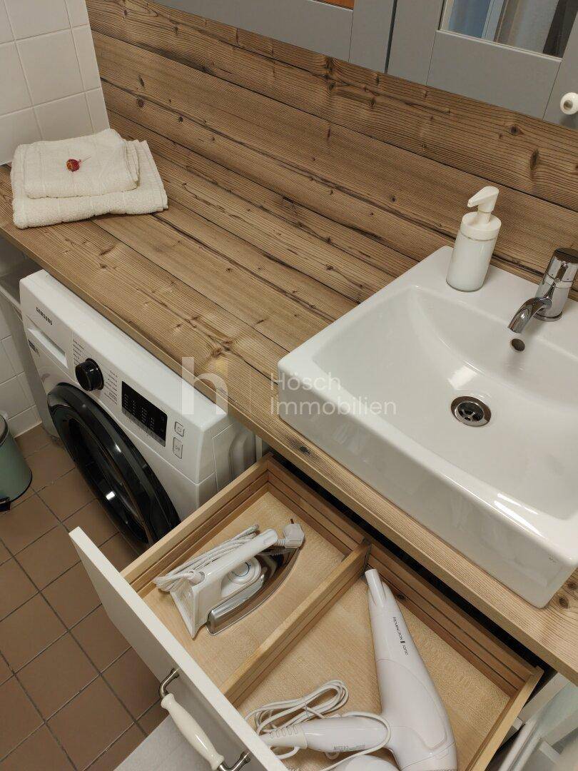 Detailansicht des Badezimmers mit Waschbecken, Waschmaschine und einer praktischen Holzablage.