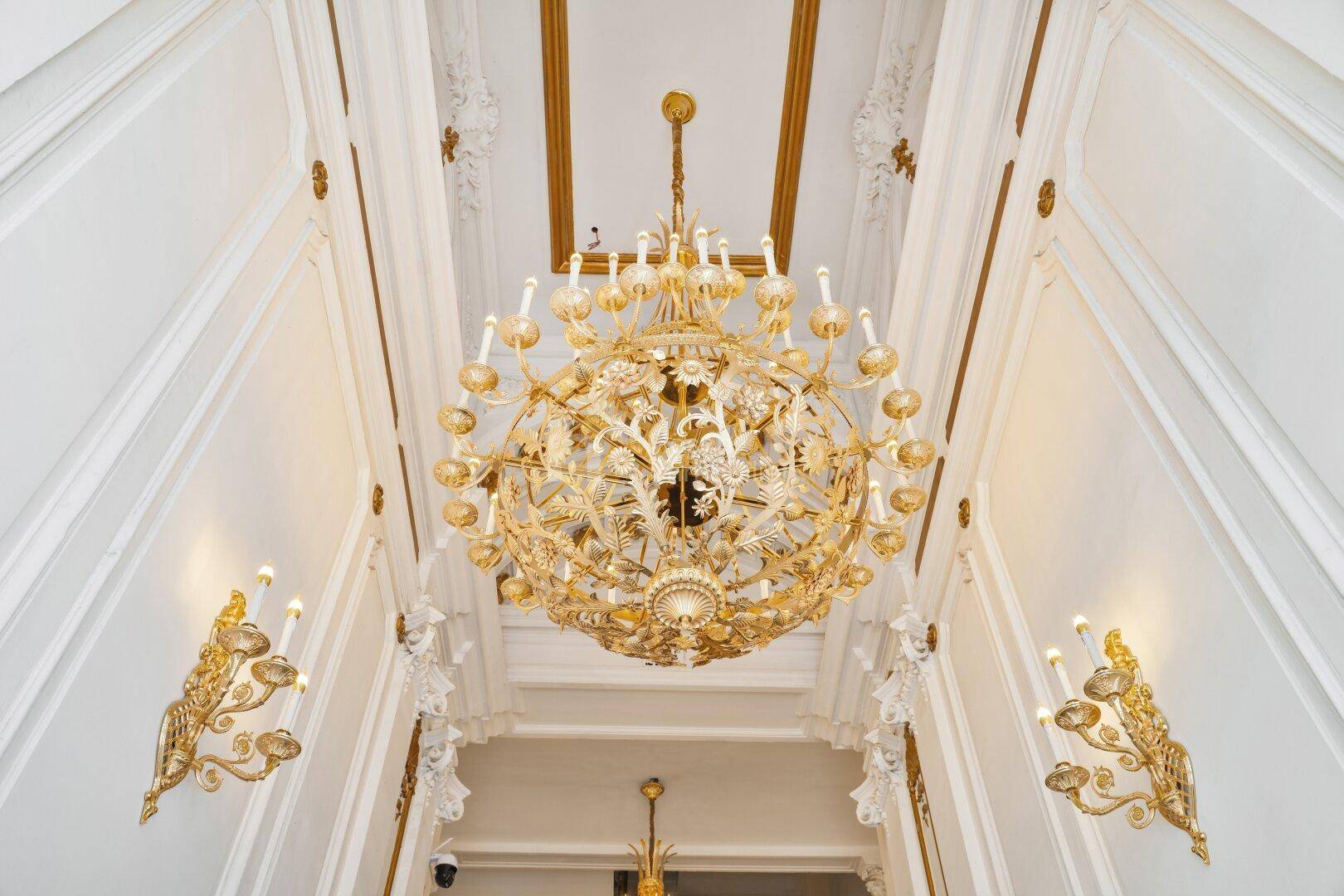 Prunkvoller goldener Kronleuchter und reich verzierte Stuckdecken in einem eleganten Eingangsbereich.