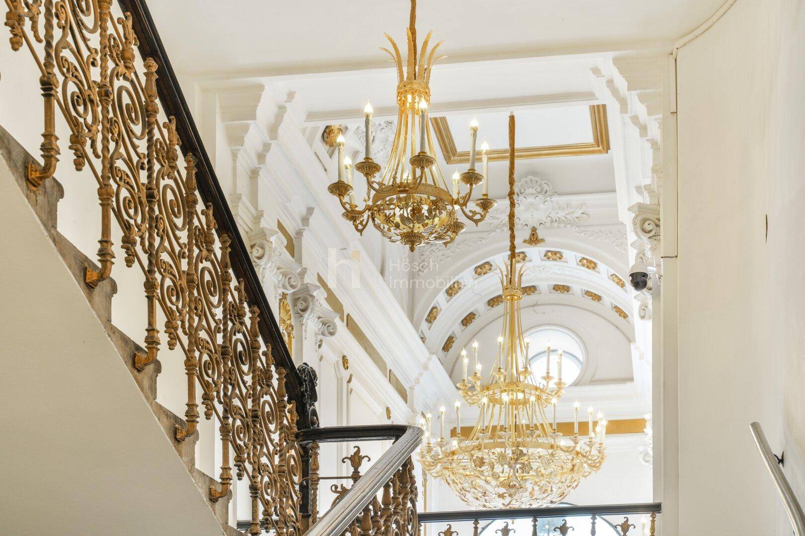 Elegantes Treppenhaus mit kunstvollen goldenen Geländern und prächtigen Kronleuchtern.