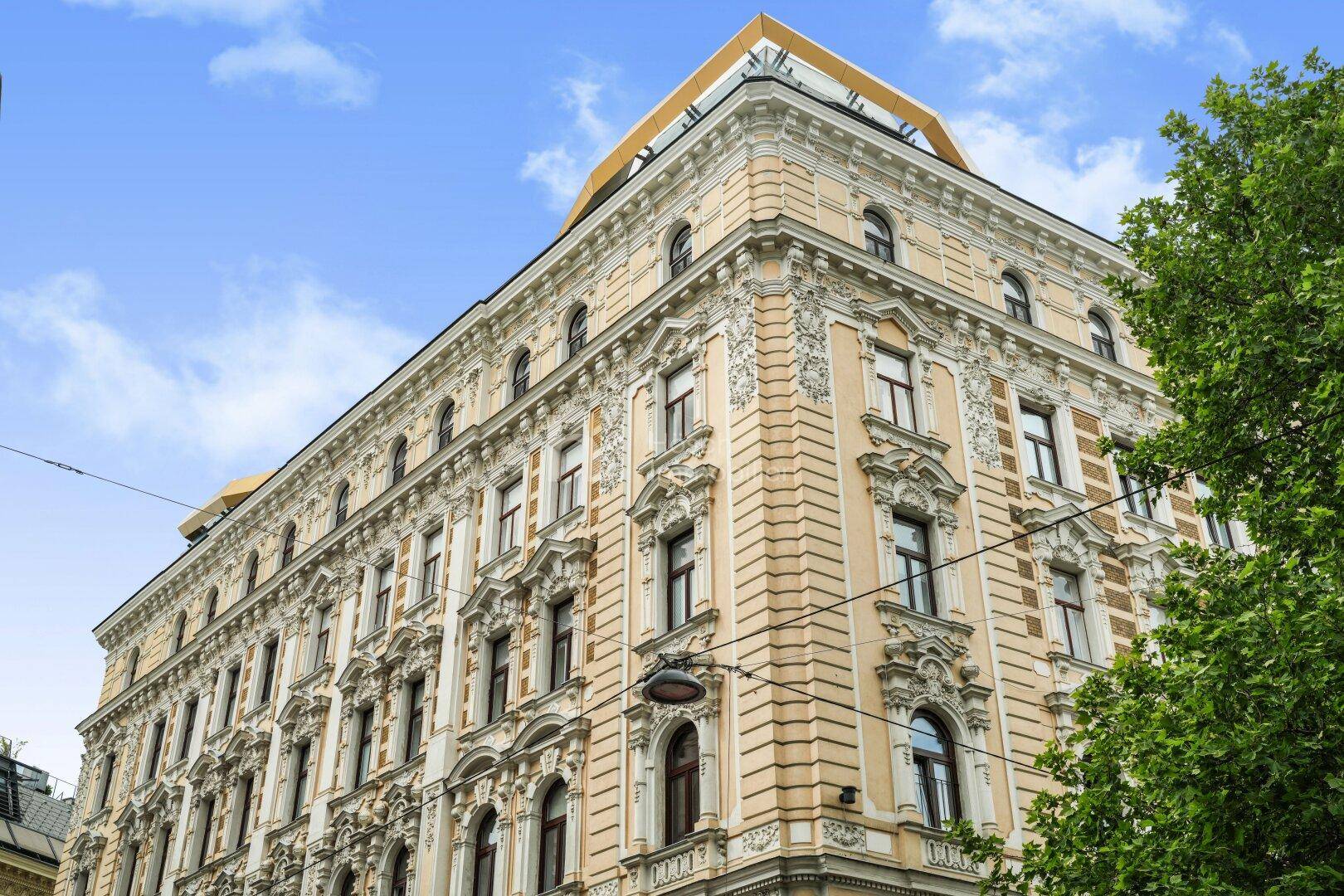 Historisches Gebäude mit reich verzierter Fassade und moderner Dachkonstruktion unter blauem Himmel.