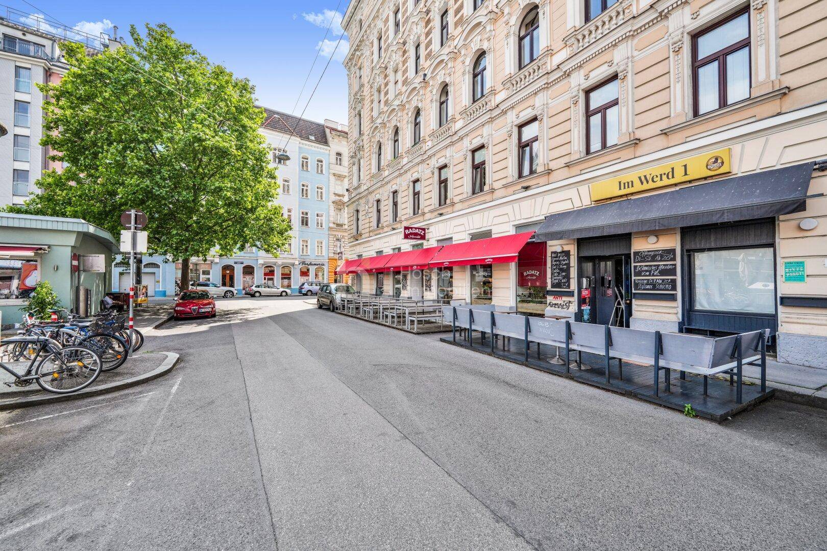 Lebendige Straße mit Geschäften, Cafés und historischen Gebäuden in urbaner Umgebung.