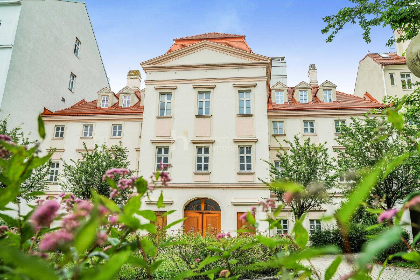 Historisches Gebäude mit blühendem Innenhof und gepflegten Grünanlagen.