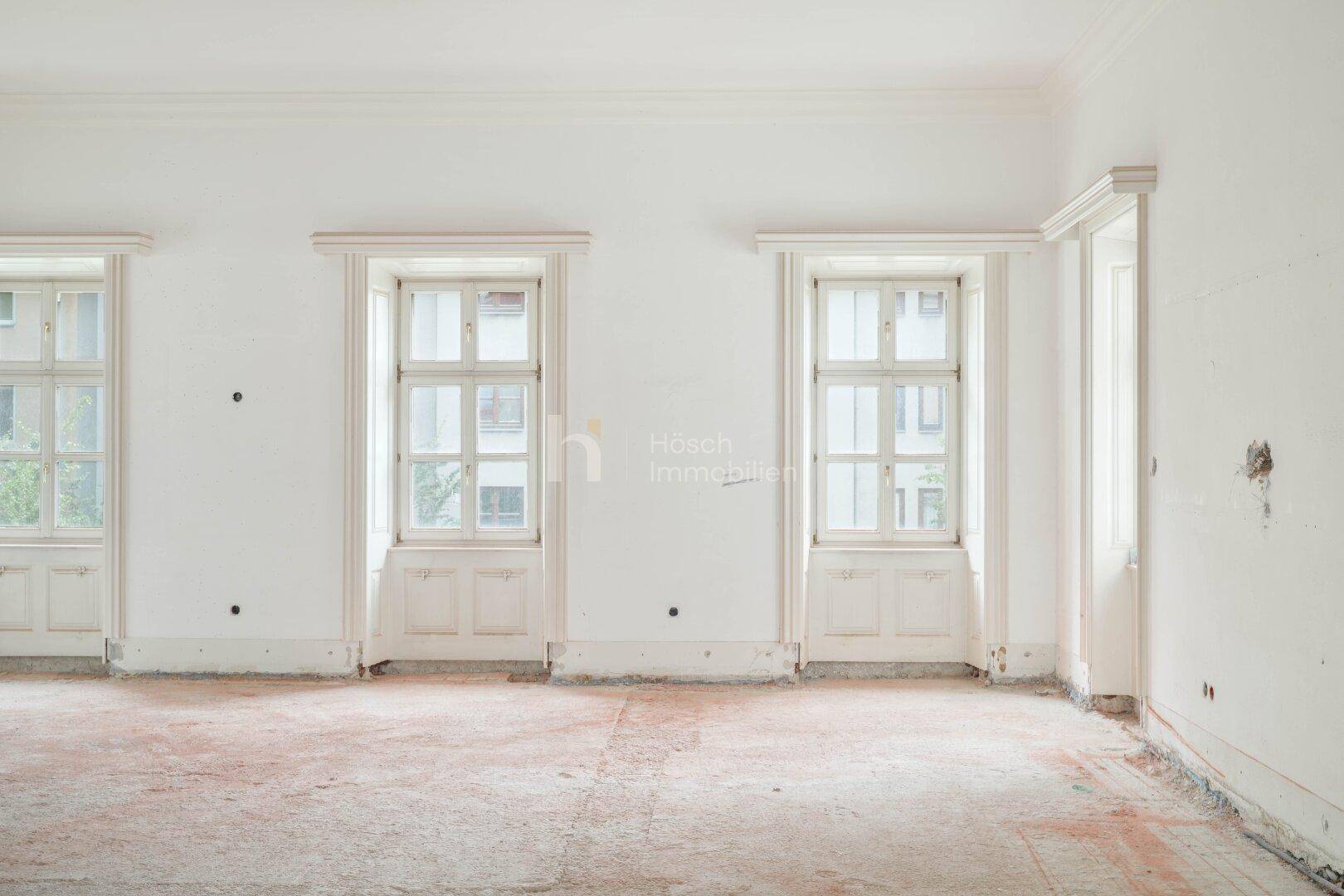 Leerer Raum mit hohen Fenstern und sichtbaren Spuren einer Renovierung.