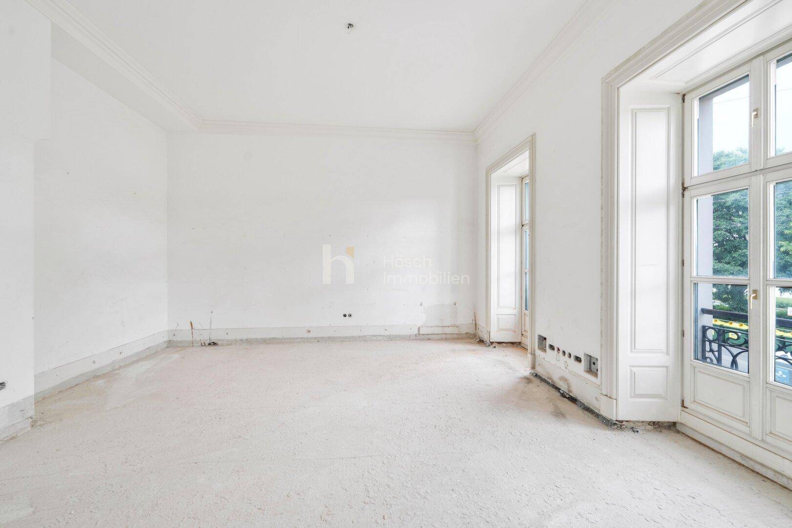 Heller, leerer Raum mit hohen Fenstertüren und Renovierungsbedarf.