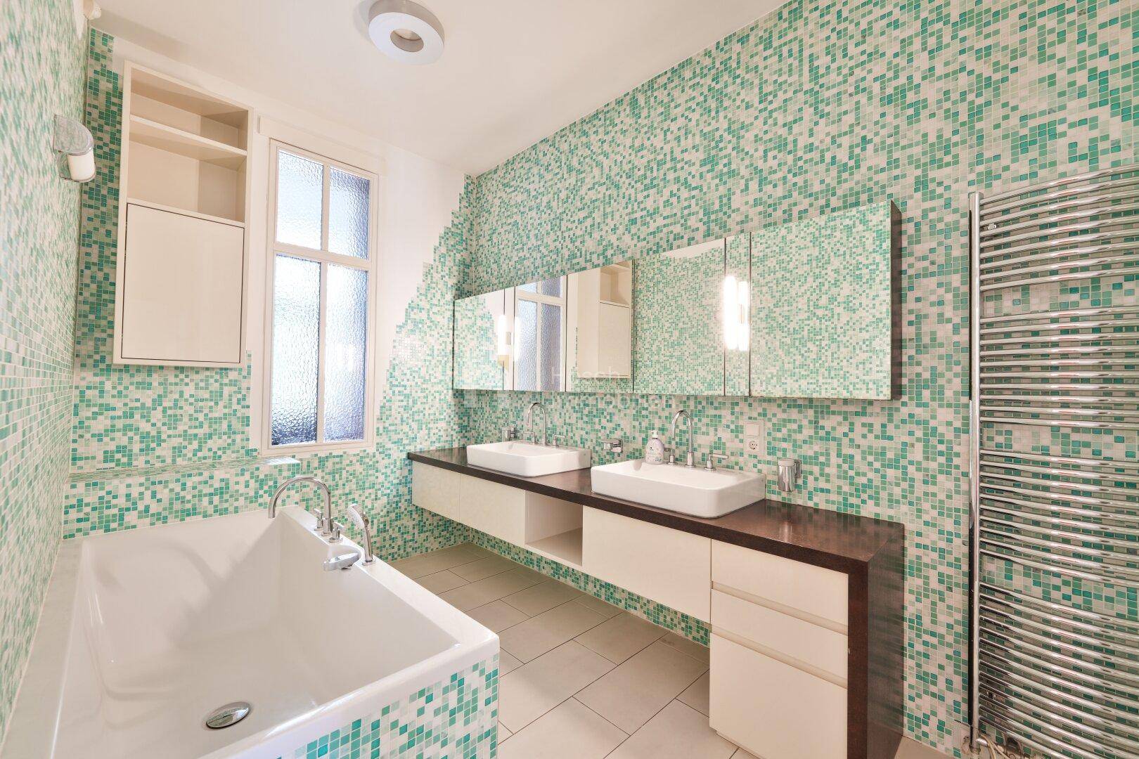 Modernes Badezimmer mit Doppelwaschbecken, Badewanne und grünen Mosaikfliesen.