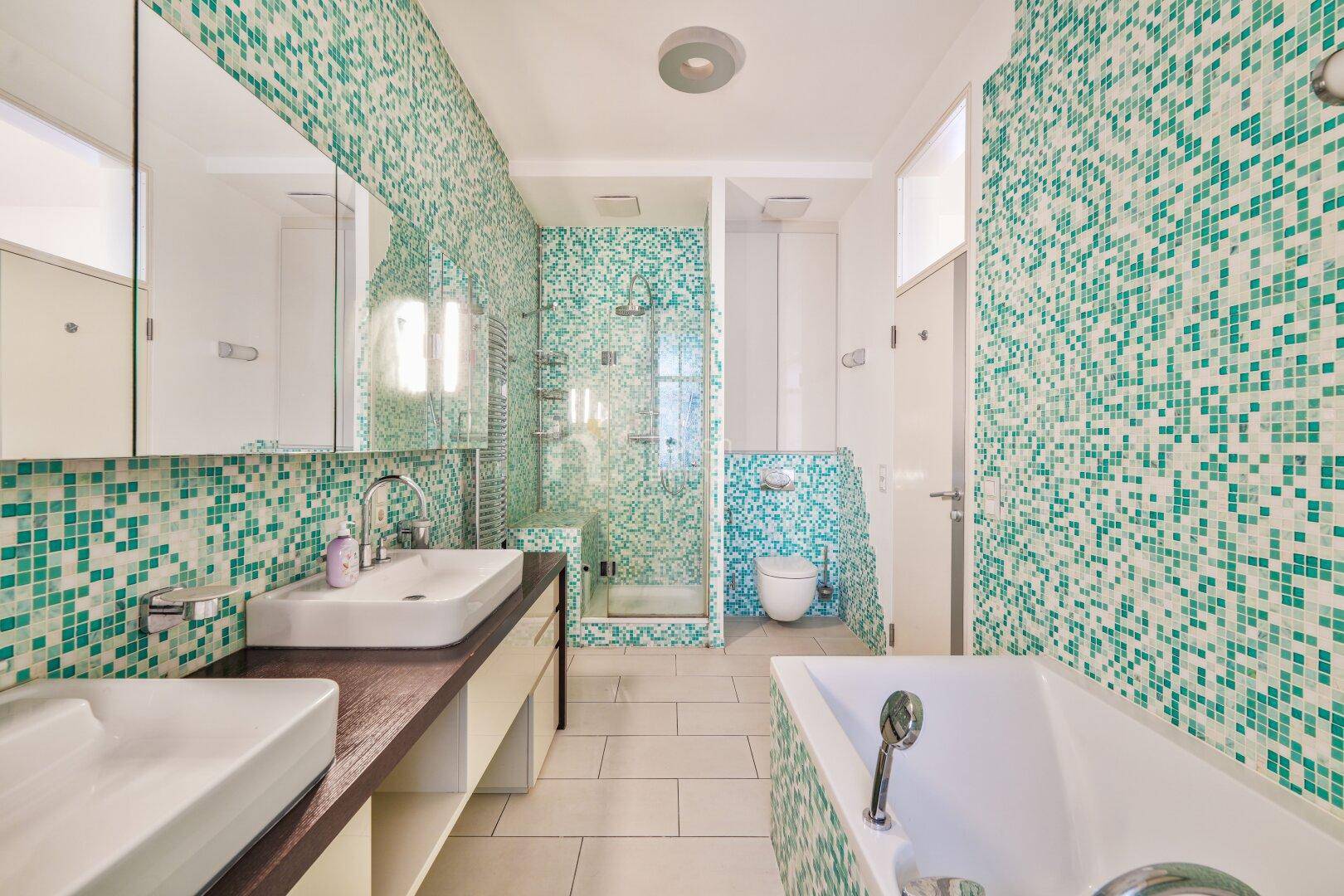 Badezimmer mit Doppelwaschbecken, Dusche, Badewanne und auffälligen Mosaikfliesen.