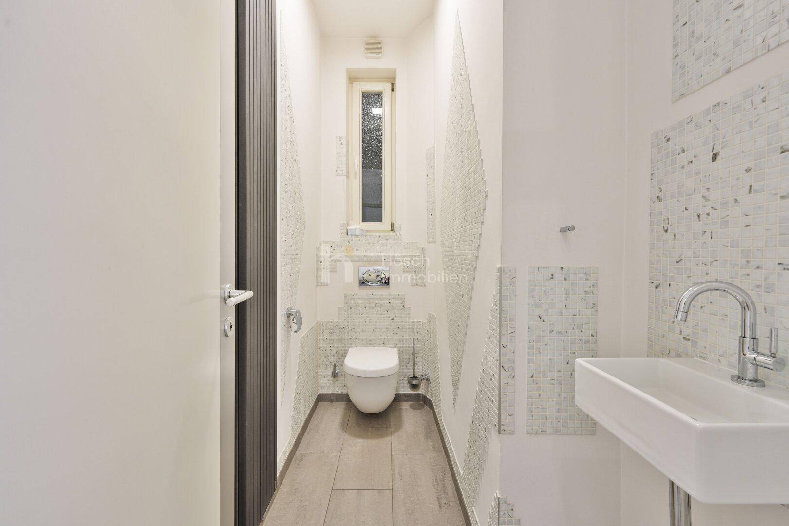 Separates Gäste-WC mit Wand-WC, kleinem Waschbecken und schmalem Fenster.