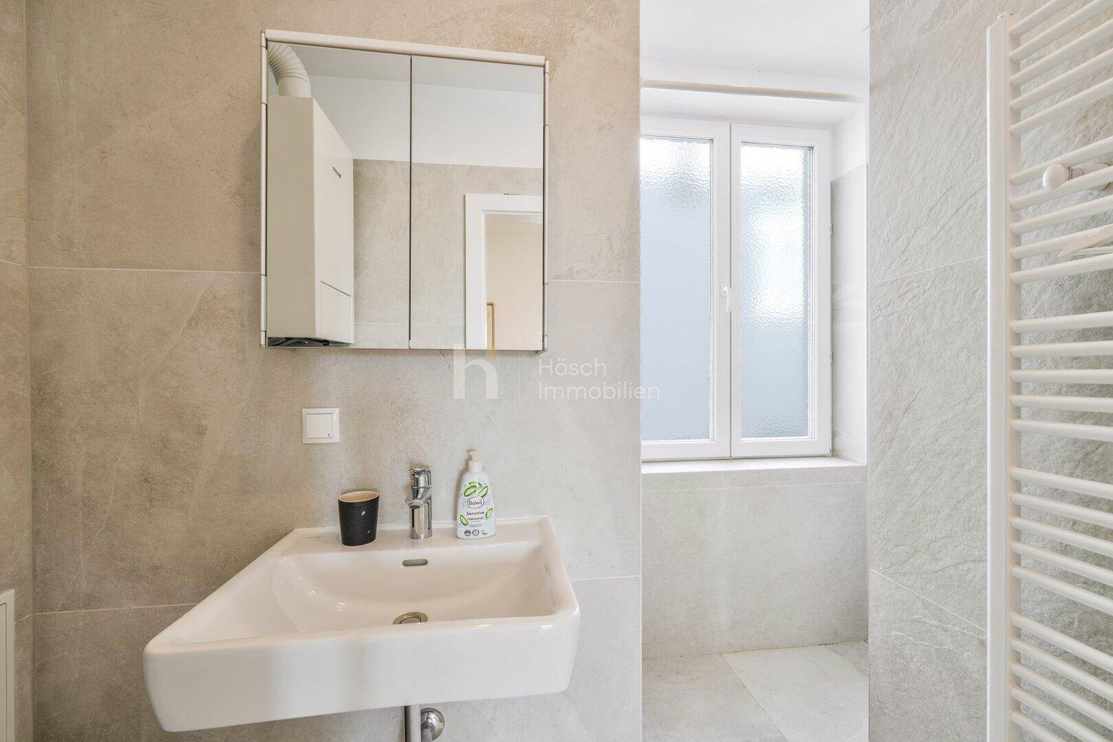 Modernes Badezimmer mit Waschbecken, Spiegelschrank und Fenster für Tageslicht.