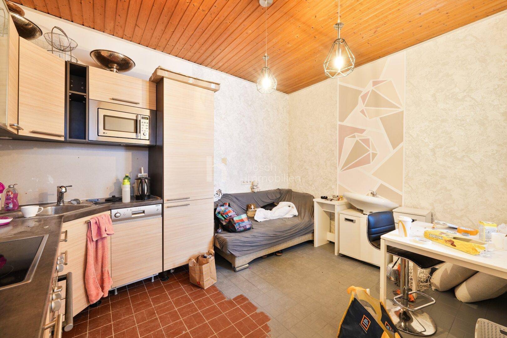Kleine Küche mit Einbauschränken, Mikrowelle und angrenzendem Wohnbereich.