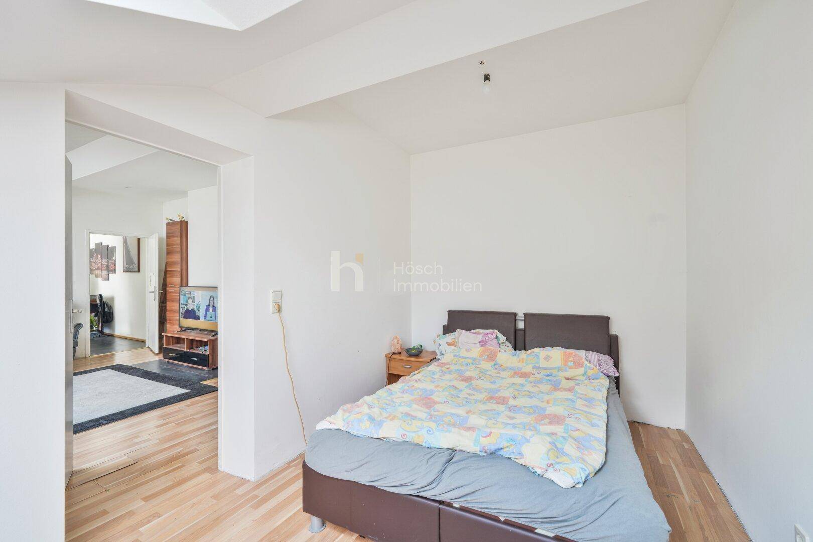 Schlafzimmer mit Doppelbett und Holzboden, angrenzend an einen weiteren Raum.