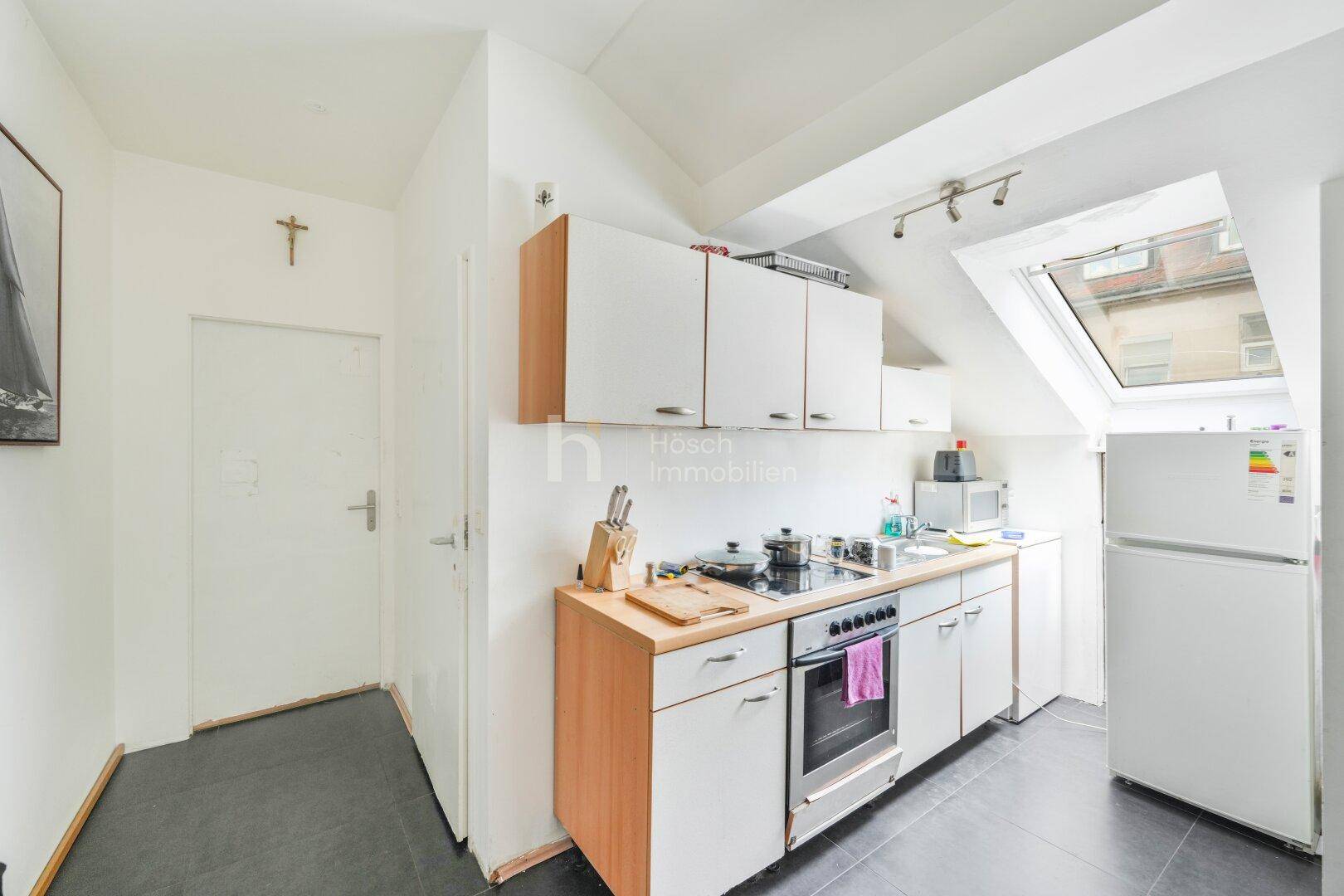 Dachgeschossküche mit Einbauschränken, Herd und Kühlschrank unter einem Dachfenster.