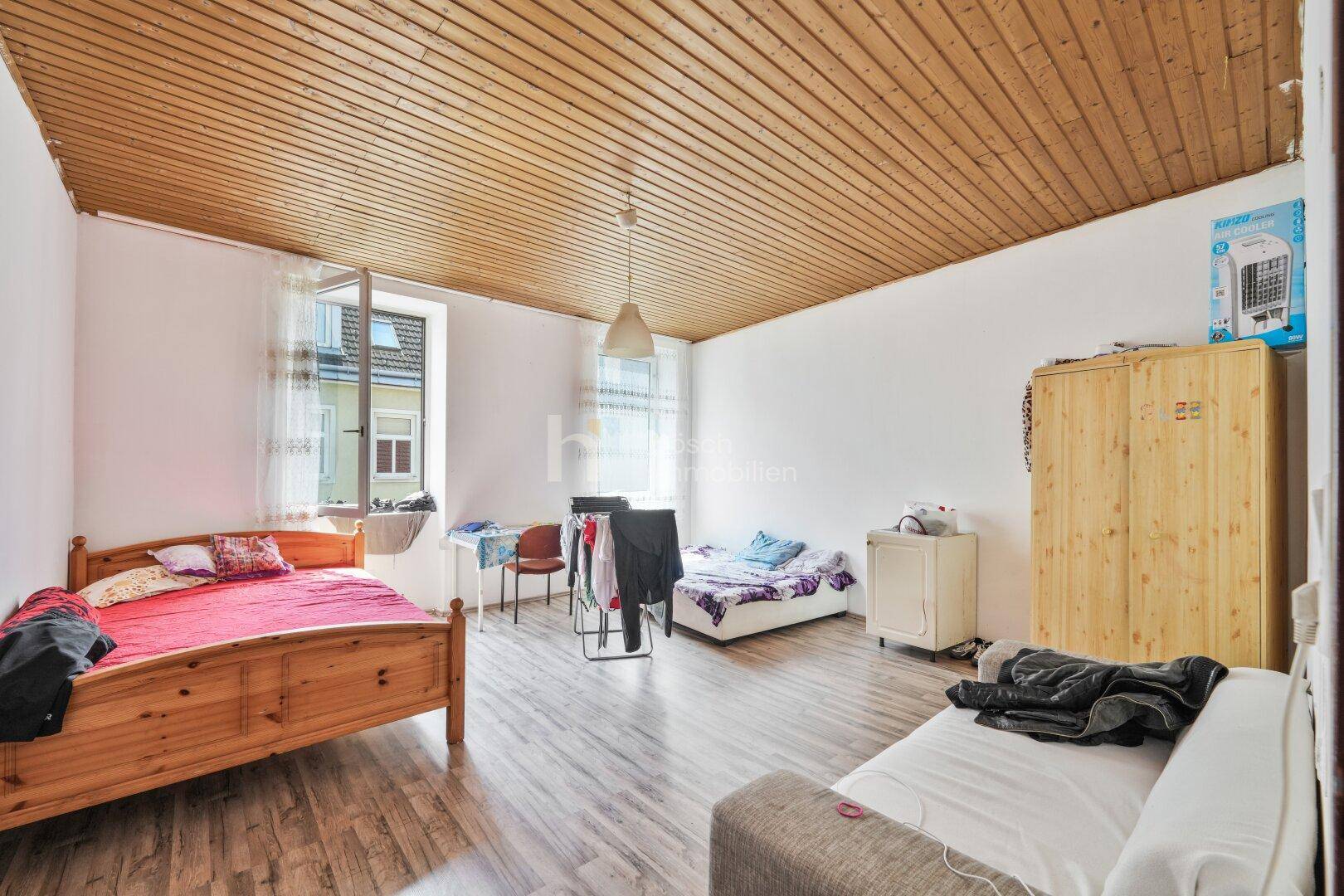 Schlafzimmer mit Holzbett, Holzdecke und Laminatboden, hell durch Fenster.