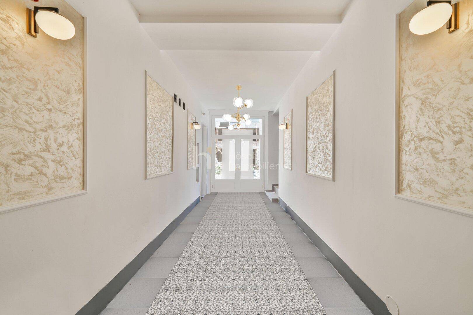 Langer, heller Flur mit gemustertem Läufer und dekorativen Wandleuchten.