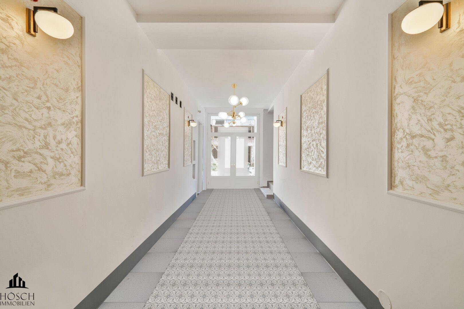 Langer, heller Flur mit gemustertem Läufer und dekorativen Wandleuchten.