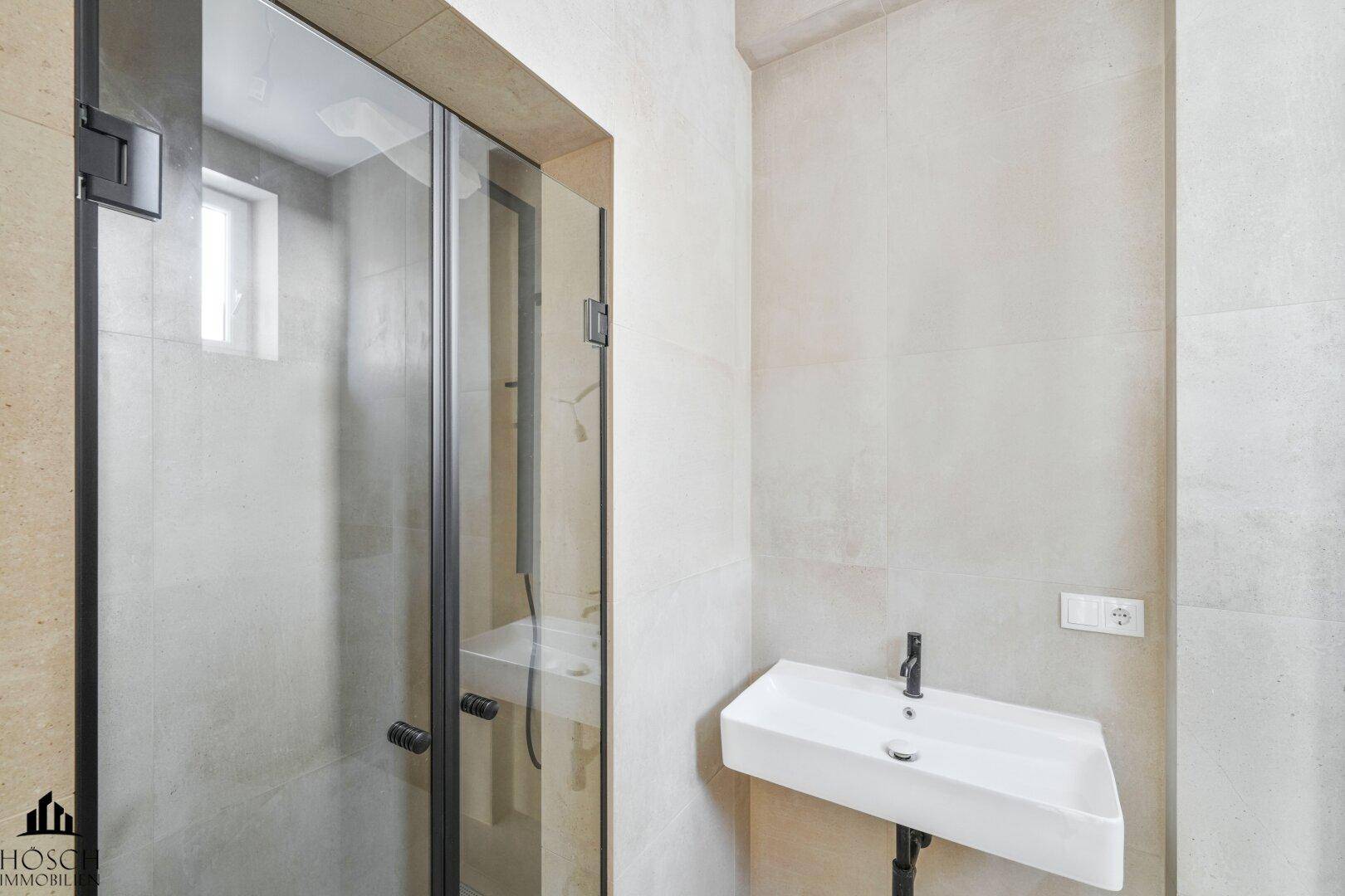 Modernes Badezimmer mit begehbarer Dusche, Waschbecken und hellen Fliesen.