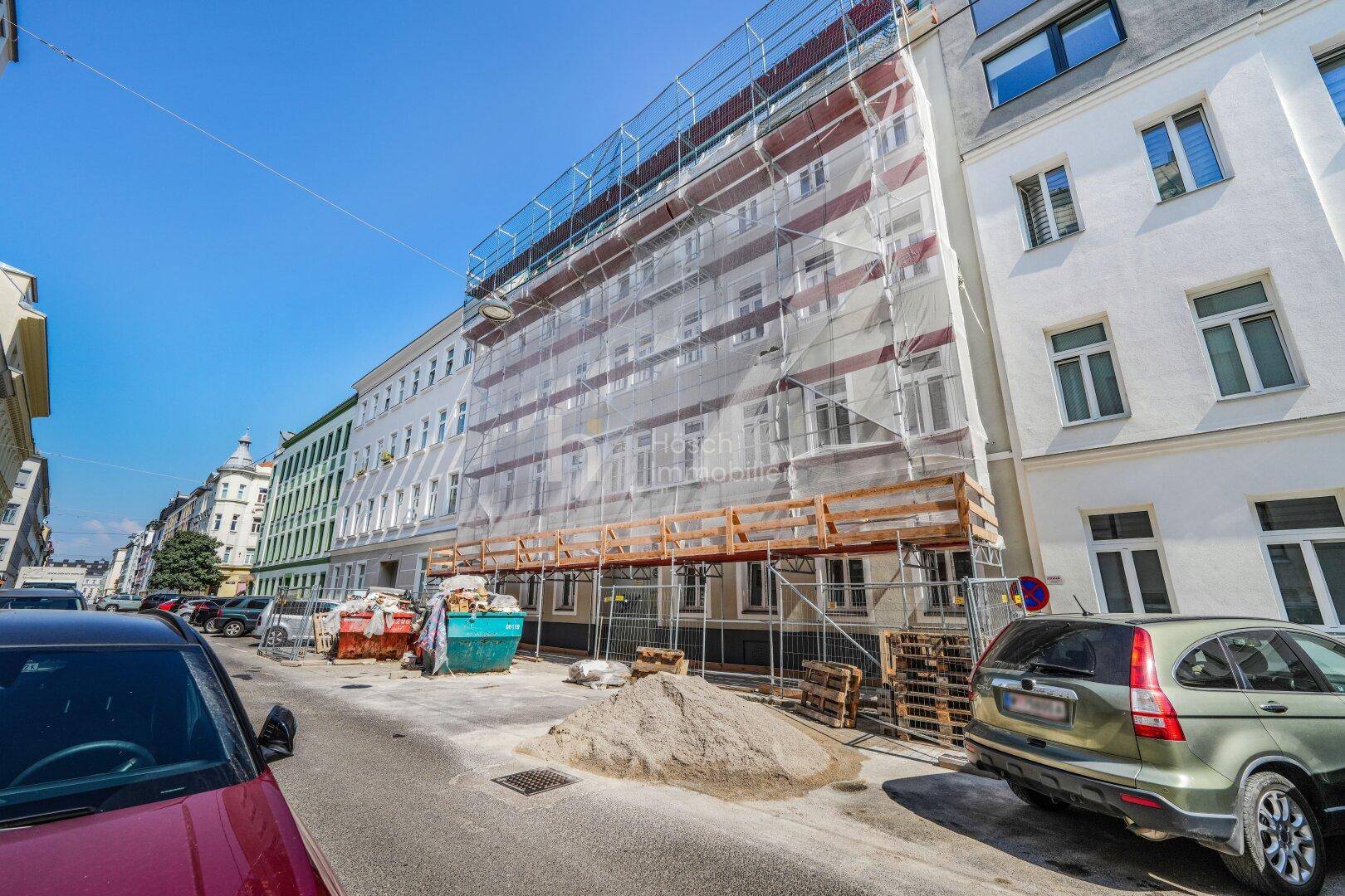 Fassade eines Gebäudes unter Gerüst mit Bauarbeiten und parkenden Autos.