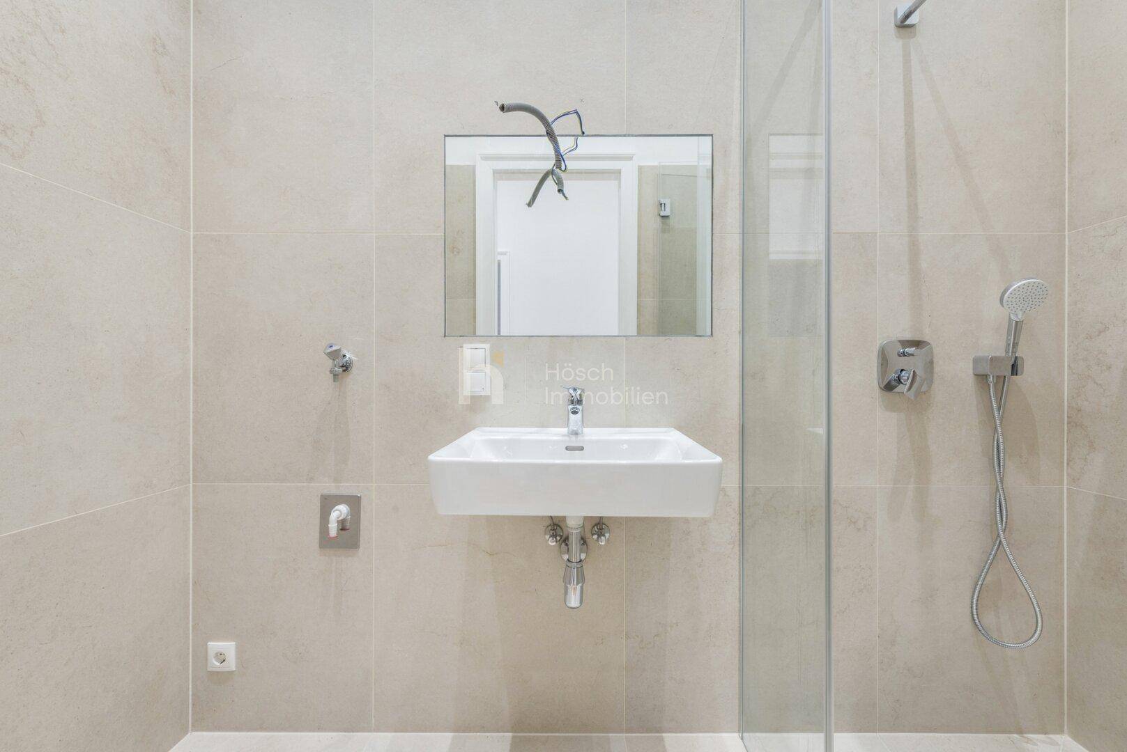 Modernes Badezimmer mit Duschbereich, Waschbecken und hellen, großformatigen Fliesen.