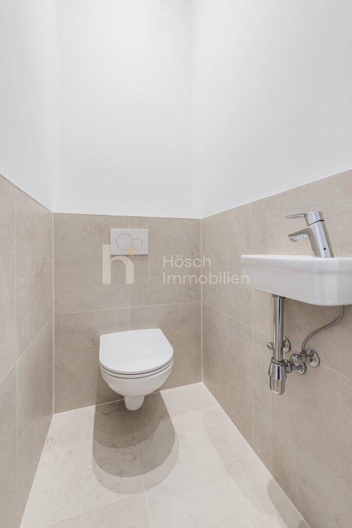 Separates Gäste-WC mit wandhängender Toilette, kleinem Waschbecken und hellen Fliesen.