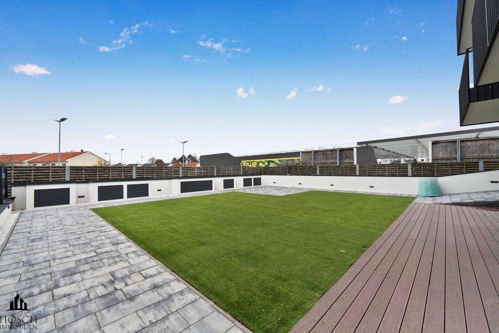 Großer Gartenbereich mit Rasenfläche und Holzdeck, ideal für Entspannung im Freien.