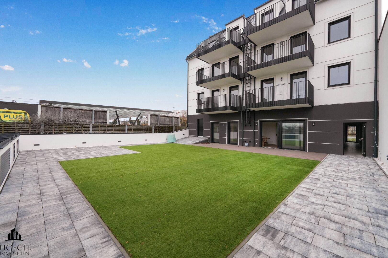 Gepflegte Grünfläche mit Rasen und gepflasterten Wegen hinter dem modernen Gebäude.