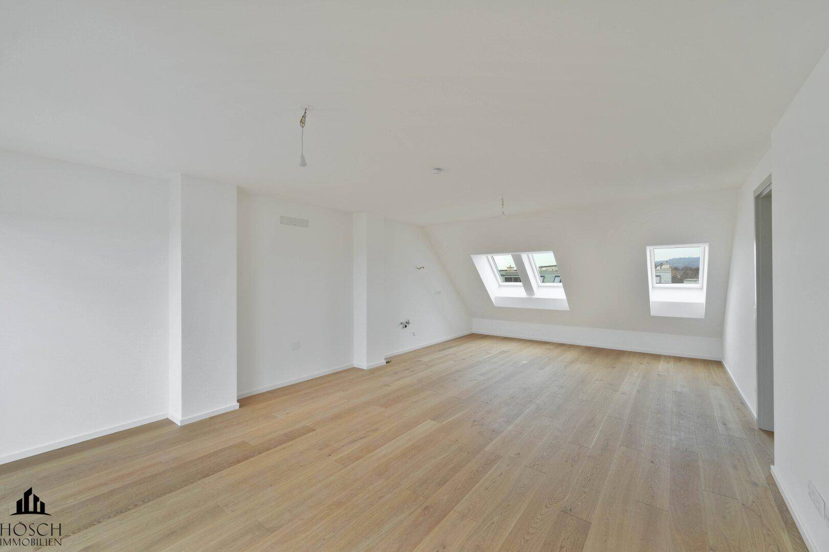 Heller, leerer Raum mit Holzboden, Dachschrägen und mehreren Dachfenstern.